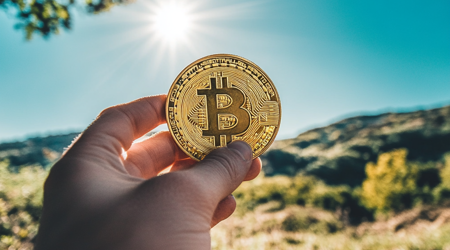 Een close-up van een hand die een bitcoin vasthoudt met een natuurlandschap in de achtergrond.