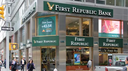 Een foto van de buitenmuur van de "First Republic Bank" in New York City, met groen-gouden letters op een roestvrijstalen gevel en digitale billboards die reclamebeelden weergeven.